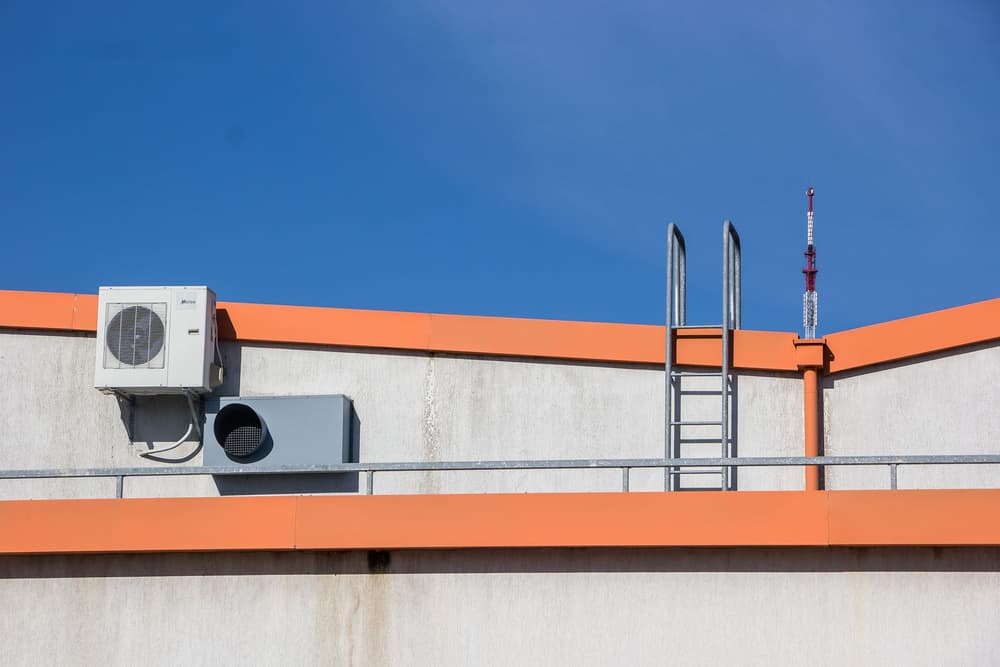 Ductless air conditioning unit mounted on a rooftop wall with a ladder beside it
