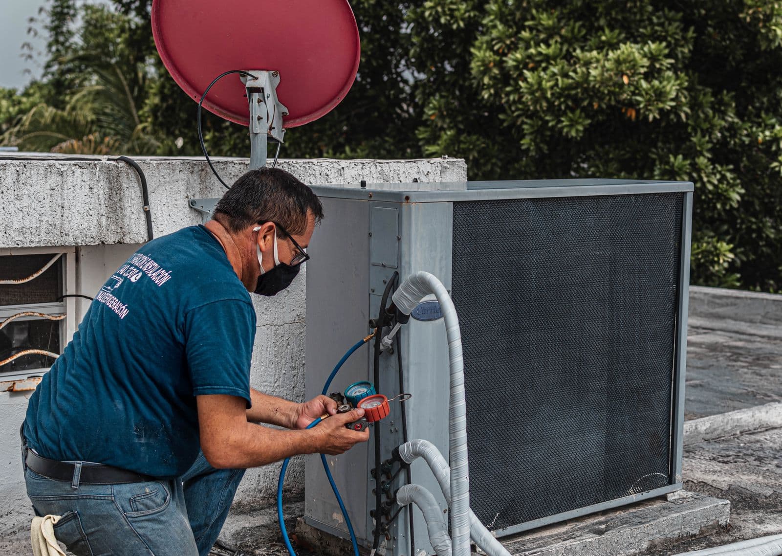 Technician in a face mask checks refrigerant gauges on an outdoor air conditioning unit on a rooftop