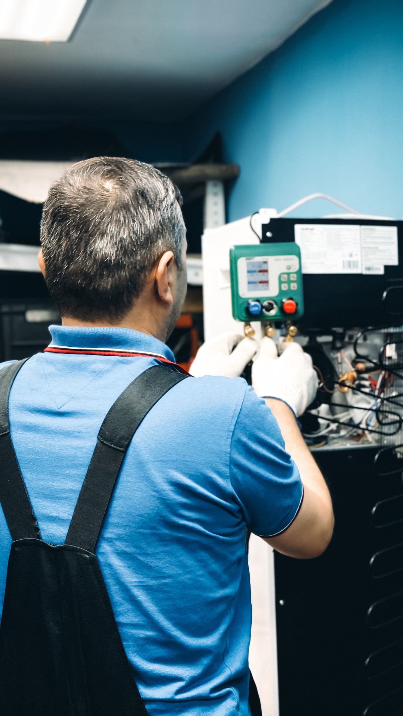 Technician seen from behind reading refrigerant gauges at an outdoor unit